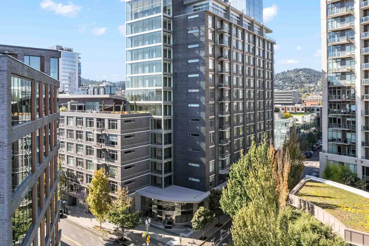A city street scene showcasing contemporary high-rise buildings, leafy trees lining the sidewalk, and active urban life—all under a bright sky. The view captures the dynamic, walkable environment surrounding the property.