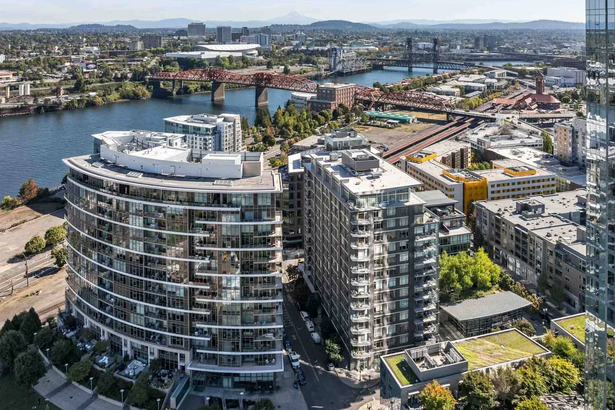 A panoramic view captures curved residential buildings along the river, with a bridge and the Pearl District’s cityscape in the background. The scene hints at the neighborhood’s proximity to waterfront leisure, community gatherings, and scenic sunset views.