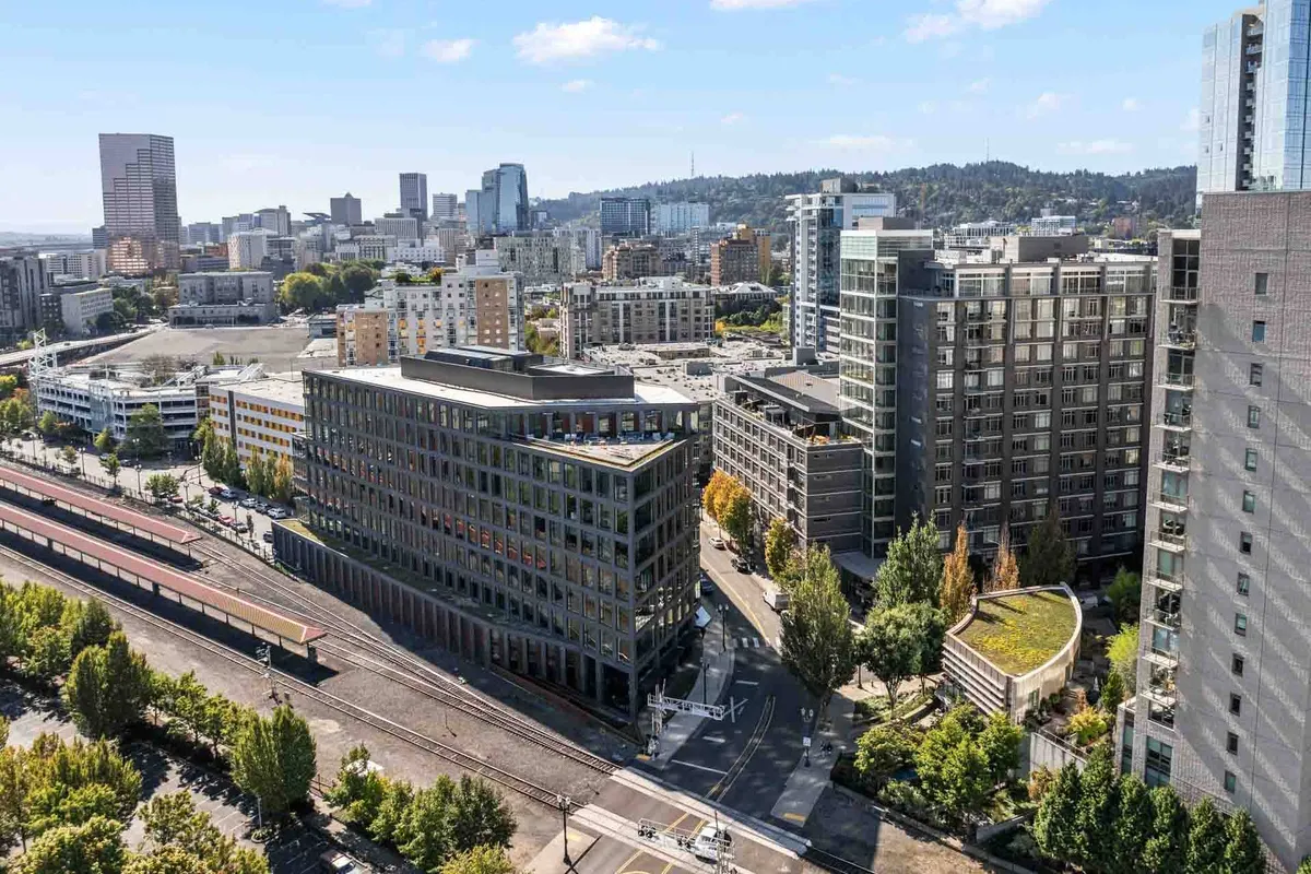 A wide-angle exterior view featuring modern buildings adjacent to generous green spaces, with the city skyline rising in the background. Well-maintained pathways weave through grassy areas, inviting urban exploration and outdoor enjoyment.