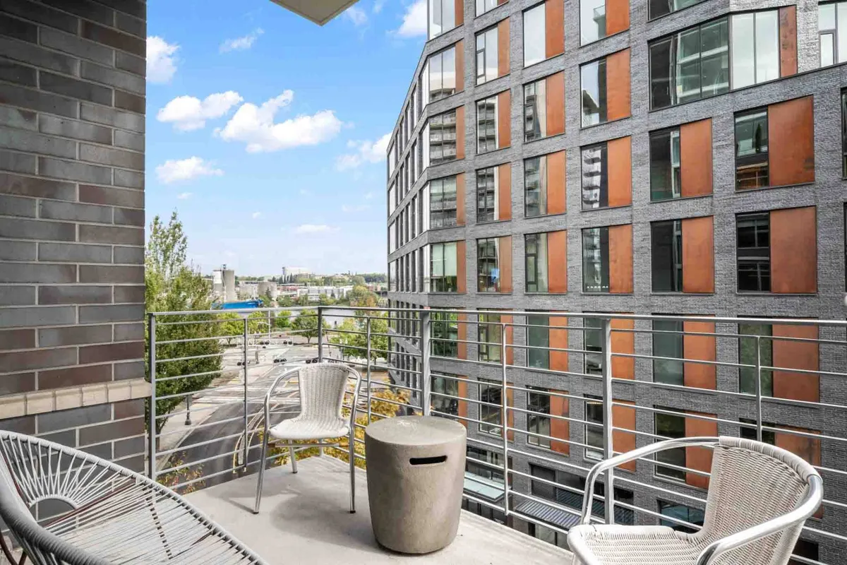 A modern balcony setup with sleek chairs and a round table, overlooking a vibrant cityscape. The scene is bathed in natural light, inviting guests to enjoy the outdoors from the comfort of the property.