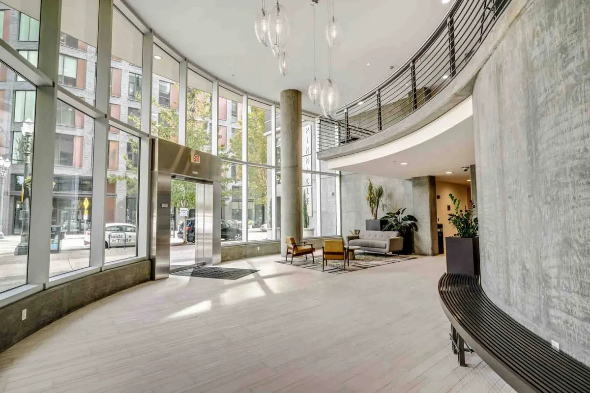This image captures a spacious, inviting condo common area with large windows, a comfortable sofa, armchairs, and vibrant indoor plants. The area is filled with natural light and has an open, welcoming feel that suggests a peaceful community environment.