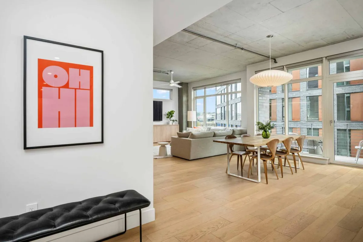 Showcasing a bright, lively dining area with colorful artwork, a dining table with chairs, a sofa in the background, and expansive windows. The space feels vibrant and lived-in, suggesting a home where both people and pets can feel comfortable.