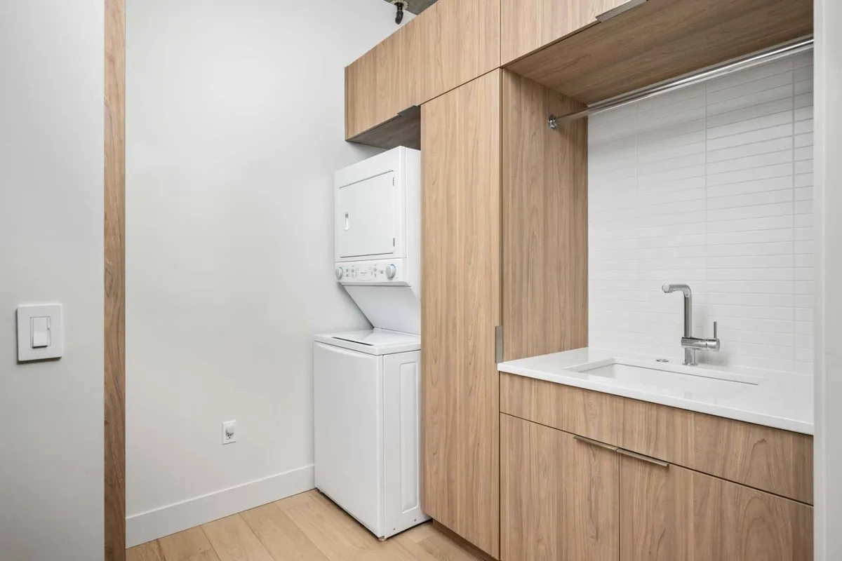 A practical utility space within the building, showcasing a washing machine, drying machine, and sink. The arrangement highlights modern conveniences often found adjacent to or accessible from garage areas in upscale urban residences.