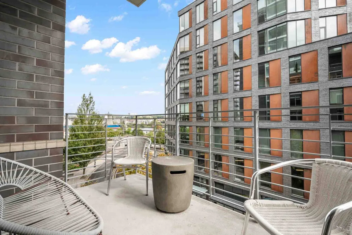 An exterior balcony with contemporary outdoor furniture, concrete table, and stylish chairs overlooks an expansive cityscape. The view allows guests to take in the vibrant life of Portland from a private, elevated setting.