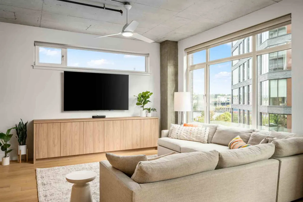 A cozy living room scene featuring a large window with city views, a comfortable sofa, and a modern TV setup. The ambiance is contemporary and relaxed, ideal for curling up after a walk with your dog.