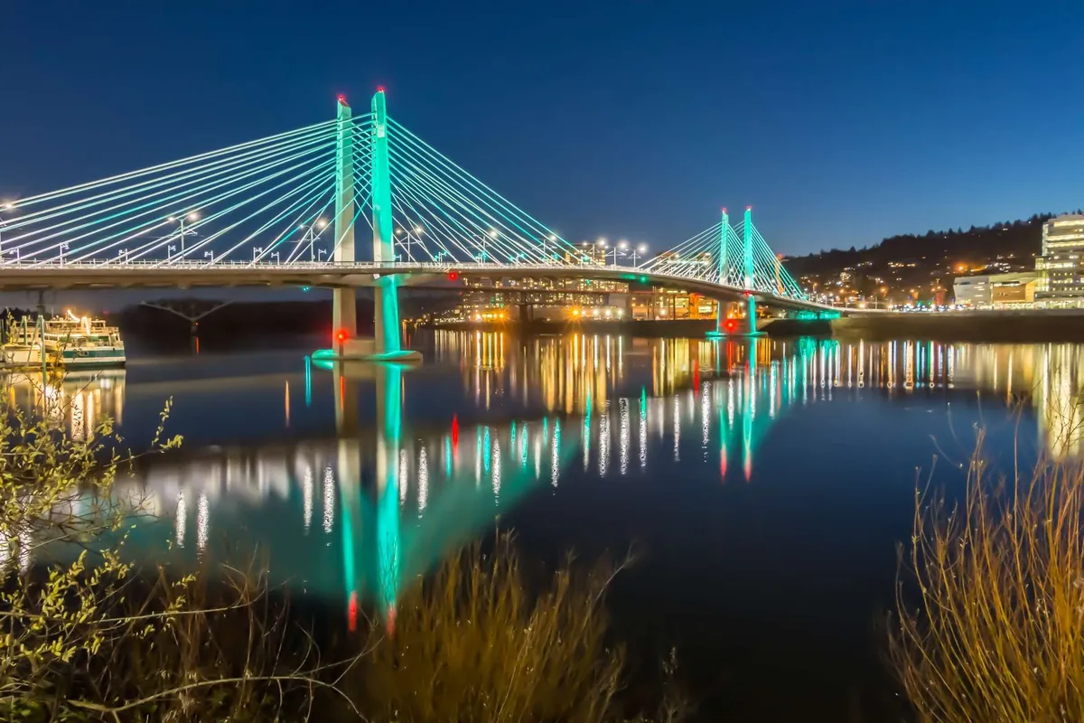 A dramatic evening scene featuring a bridge over the river, reflected city lights shimmering in the water, and a lively yet serene atmosphere ideal for exploration or after-hours strolls.