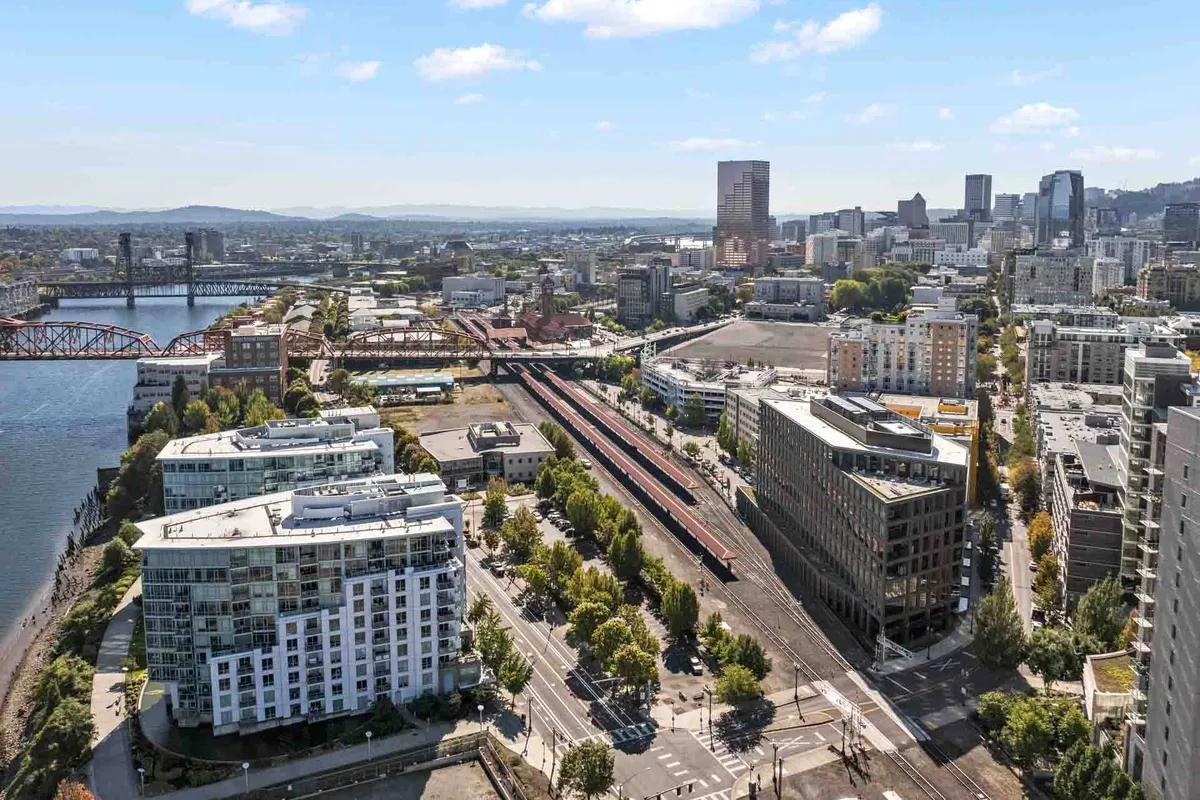 The vibrant Portland waterfront with a sweeping view of the river, city skyline, and bridges. The area bustles with people strolling along the waterfront and enjoying nearby urban parks and cafes.