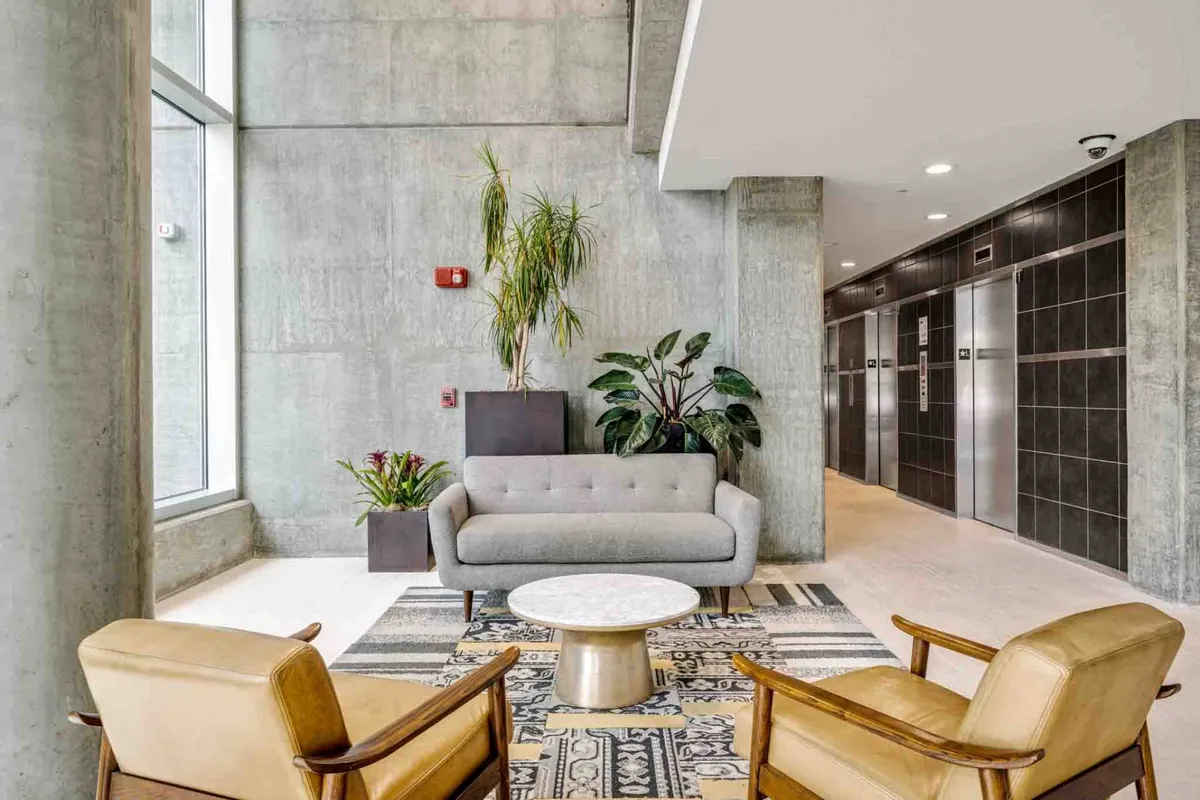 A contemporary and inviting lobby scene featuring plush seating, a coffee table, decorative plants, and elevators in the background. The area is well-lit and welcoming, giving visitors and residents a sense of comfort and security as they transition from the garage to the rest of the building.